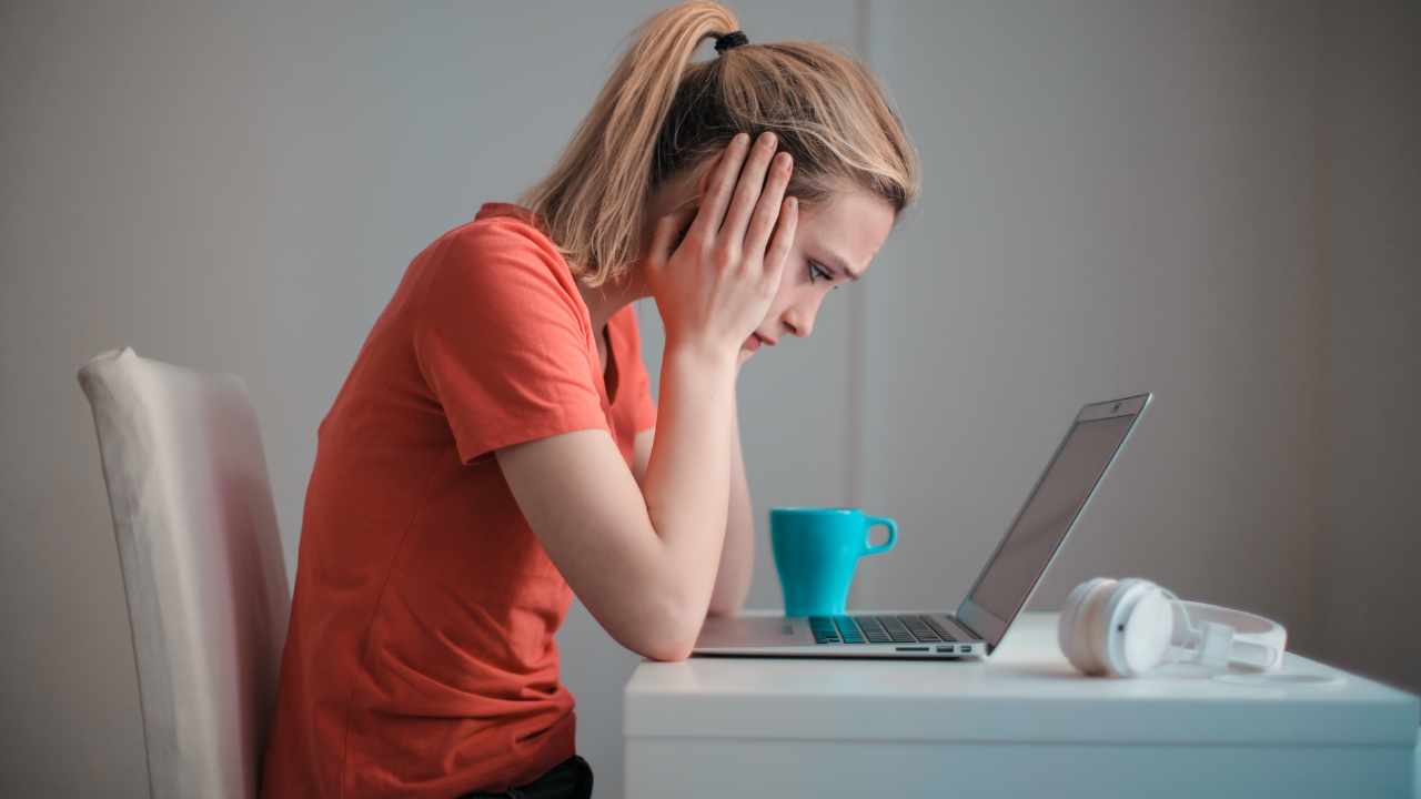 A girl is looking into laptop screen holding her head with both hands